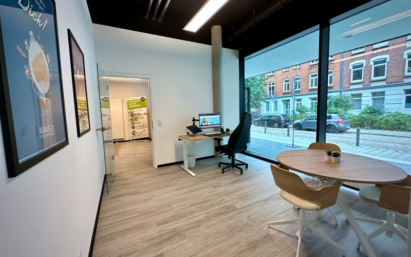 Blick in den hellen Büroraum in Kiel mit Arbeitsplatz, Besprechungstisch und großer Fensterfront zur Straße